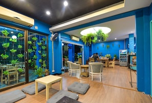 A modern indoor space with blue walls, wooden flooring, and a variety of seating arrangements including tables and chairs. - BGW Phuket - Hostel (Patong)