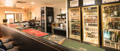 Zona de bar con mostrador, asientos y estantes refrigerados llenos de bebidas.