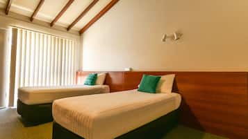 A hotel room with two beds, wooden headboards, and a window with blinds.