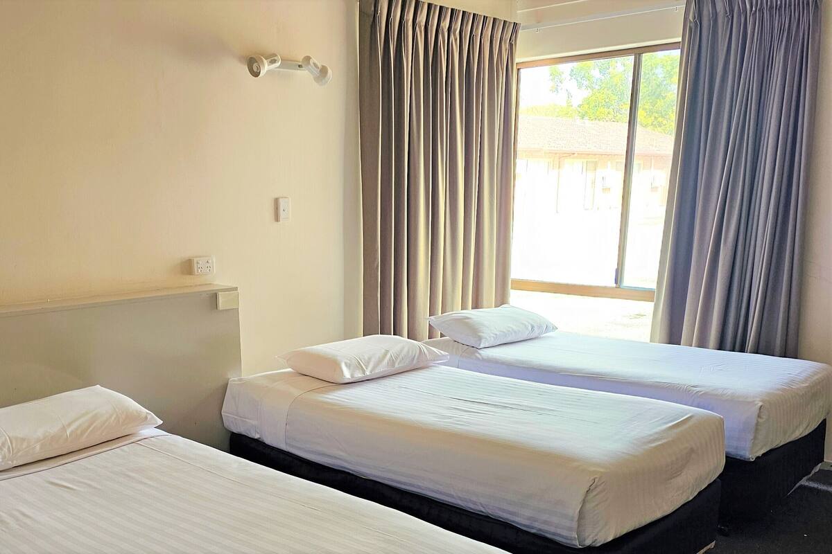 A hotel room with two beds, a window with curtains, and a wall-mounted light fixture.