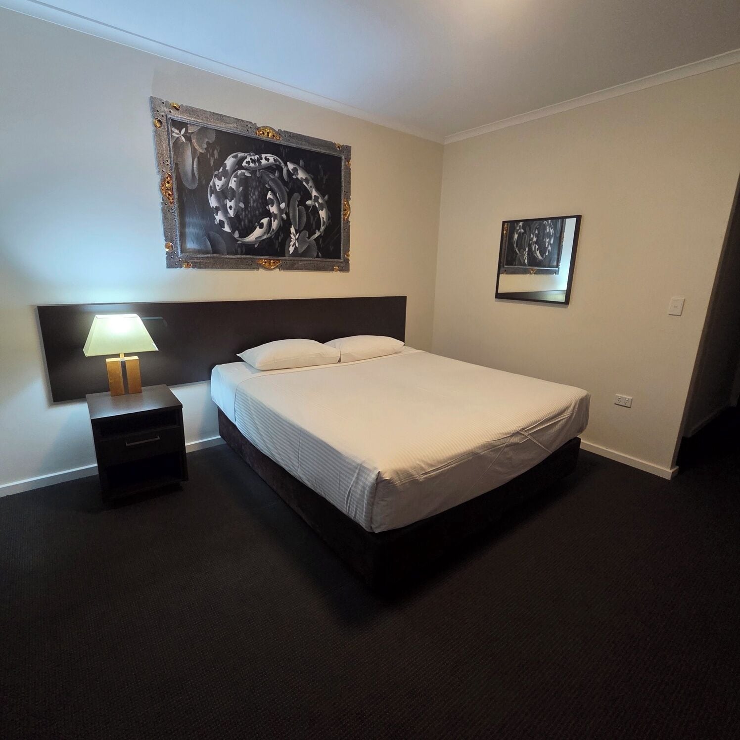 A hotel room with a bed, a nightstand with a lamp, and two framed pictures on the wall.