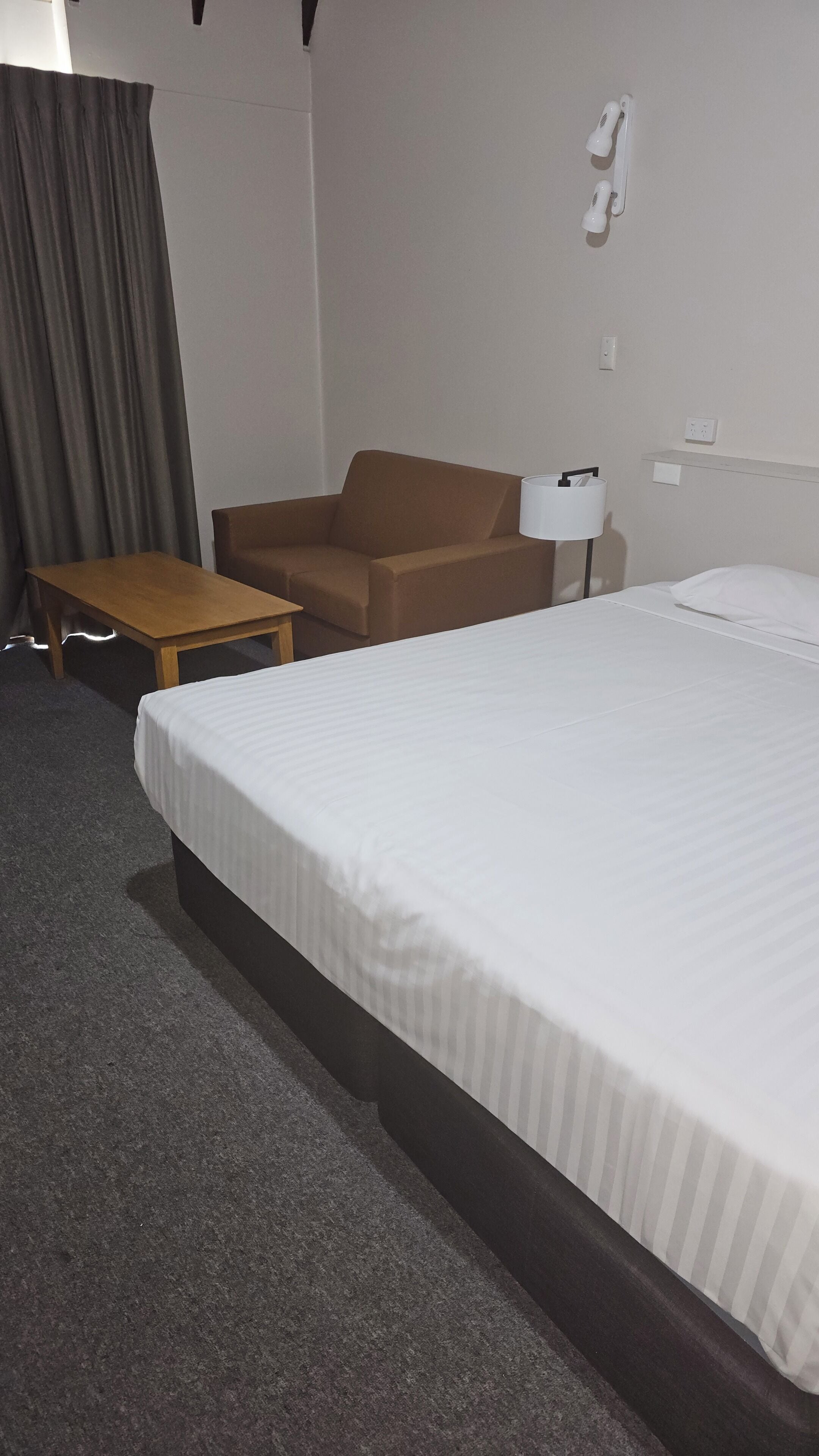 A hotel room with a bed, a sofa, a small table, and a lamp.