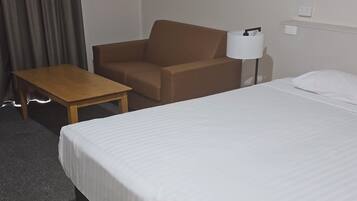 A hotel room with a bed, a sofa, a small table, and a lamp.