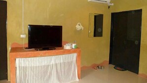Una habitación con una televisión sobre un soporte de madera, una cortina blanca, una mesita con una vela y una puerta negra.
