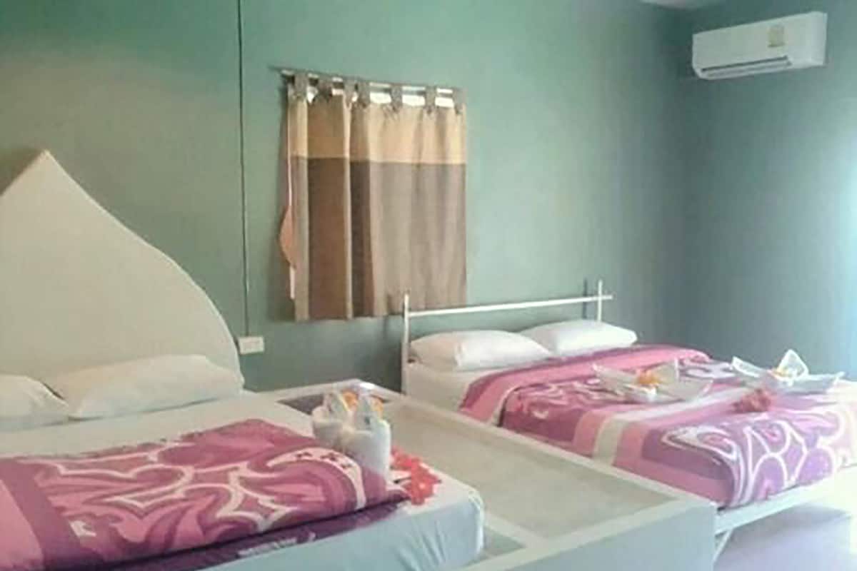 Una habitación de hotel con dos camas, cada una con cabecero blanco, ropa de cama estampada en rosa y blanco, y una mesita con una botella y una flor.
