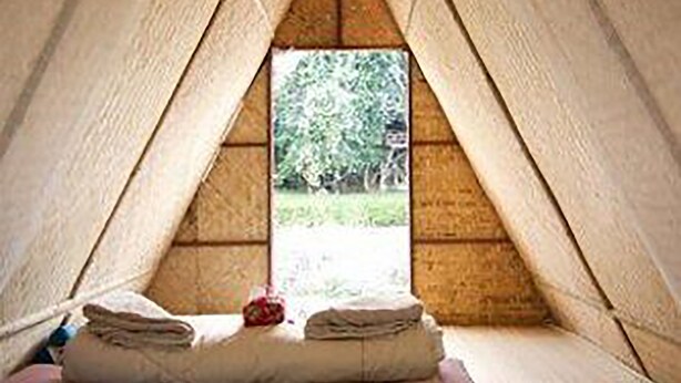 Una habitación acogedora de forma triangular con una cama, almohadas y una ventana con vistas a la vegetación.