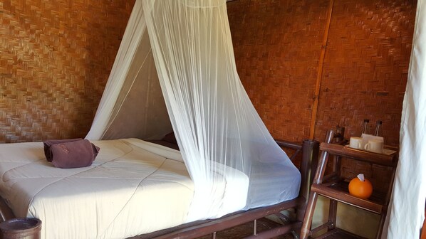Quarto com cama, mosquiteiro, parede de madeira e prateleira com produtos de higiene pessoal.