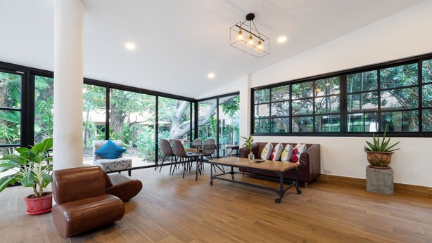 Une pièce spacieuse avec de grandes fenêtres, un plancher en bois, un canapé en cuir marron, une table à manger avec des chaises et une plante en pot.