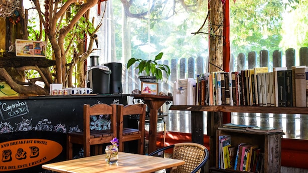 A cozy cafe with a wooden table, chairs, a bookshelf, and a chalkboard menu. - B&B Hostel (Punta del Este)
