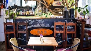 A rustic outdoor seating area with wicker chairs and a wooden table, a chalkboard menu, and a variety of bottles and plants on the counter. - B&B Hostel (Punta del Este)