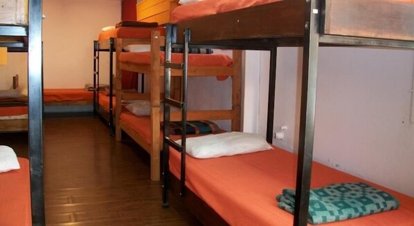 A dormitory room with bunk beds, wooden floors, and orange bedding.