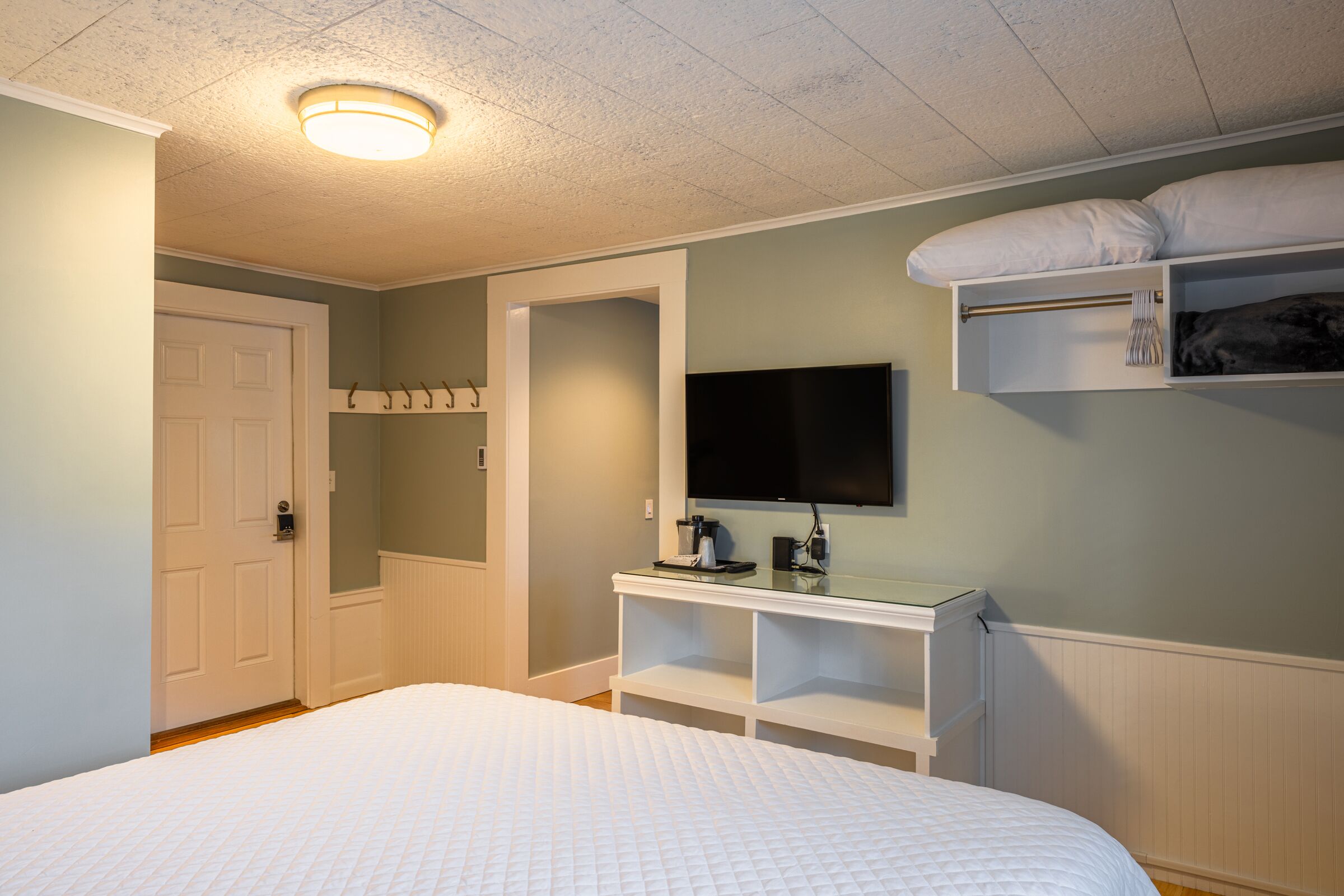 A bedroom with a bed, a television mounted on a wall, a coat rack, and a storage shelf.
