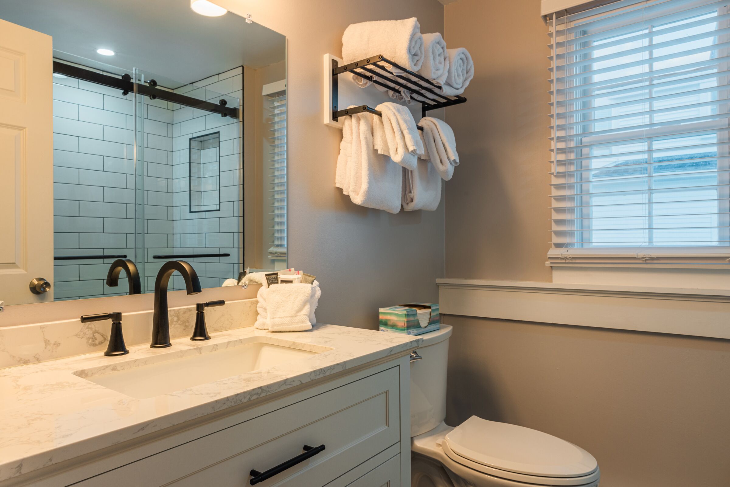 A bathroom with a marble sink, black faucets, a towel rack, and a toilet.
