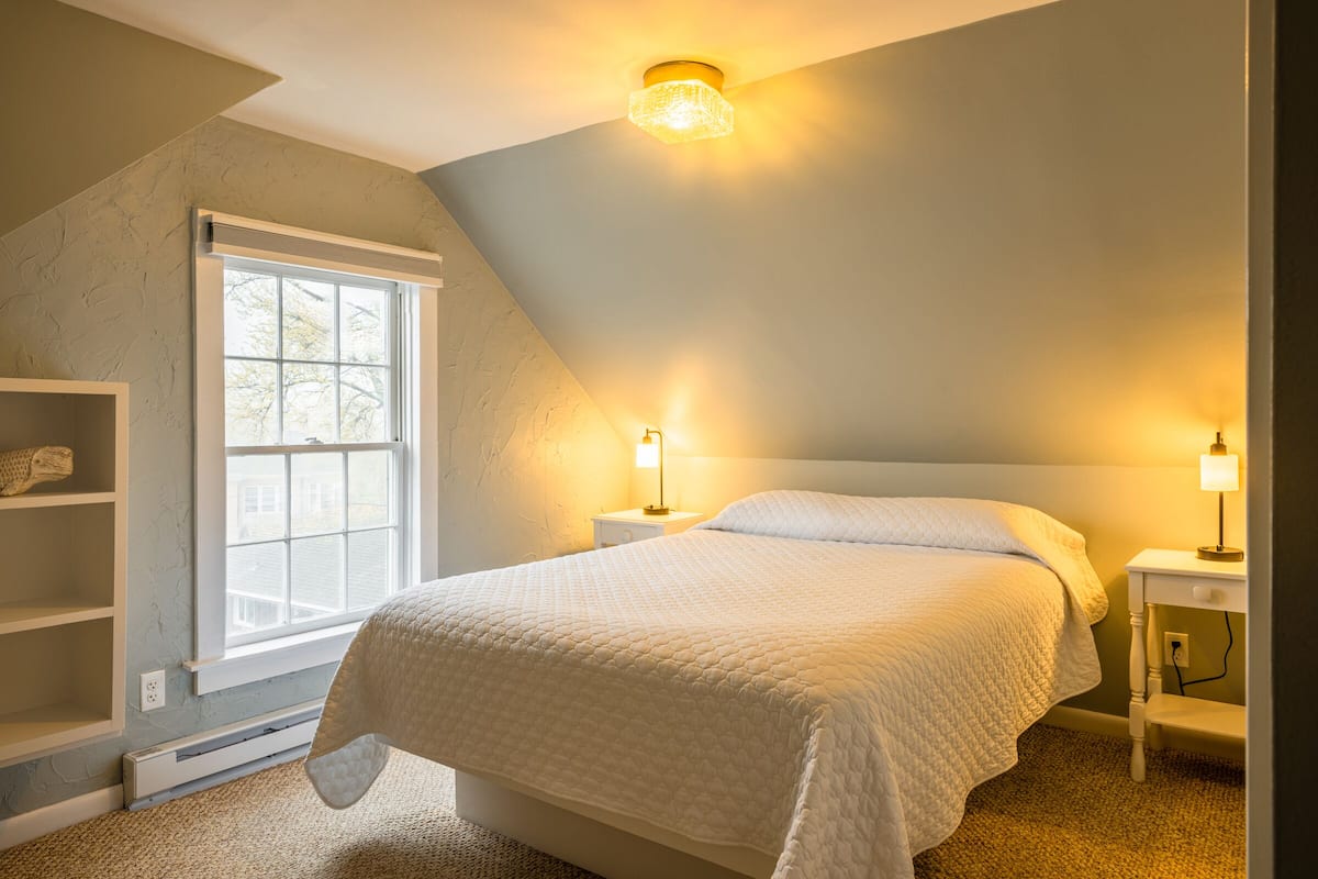 A bedroom with a large bed, a window, and two bedside lamps.