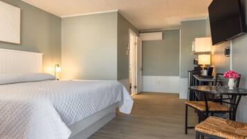 Habitación de hotel con cama, una mesa de comedor con sillas, televisor montado en la pared y una puerta que da a otra habitación.
