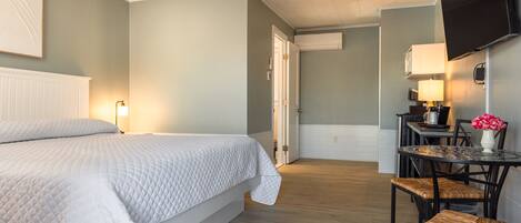 Une chambre d’hôtel comprenant un lit, une table à manger avec des chaises, un téléviseur fixé au mur et une porte donnant sur une autre pièce.