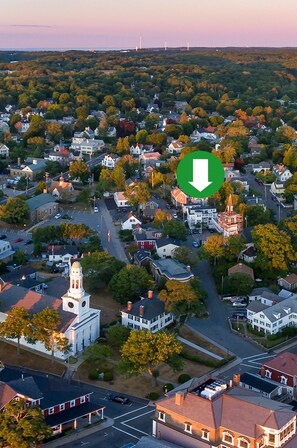 An aerial view of a town with a prominent church, residential houses, and a large green arrow pointing downwards. - Eagle House Motel (Rockport)
