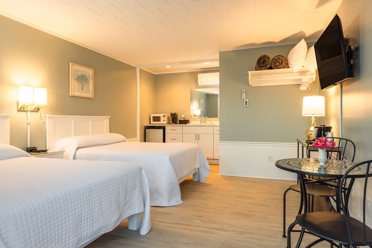 A hotel room with two beds, a dining table with chairs, a microwave, a sink, and a television mounted on the wall.