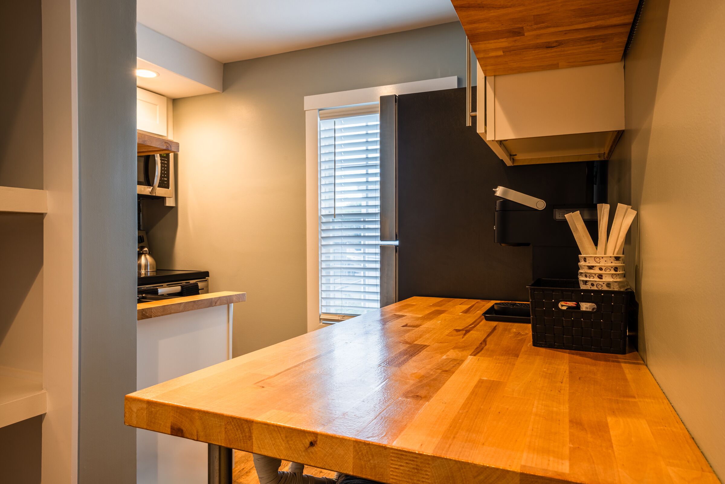 A compact kitchen with a wooden countertop, a microwave, and a black storage bin.