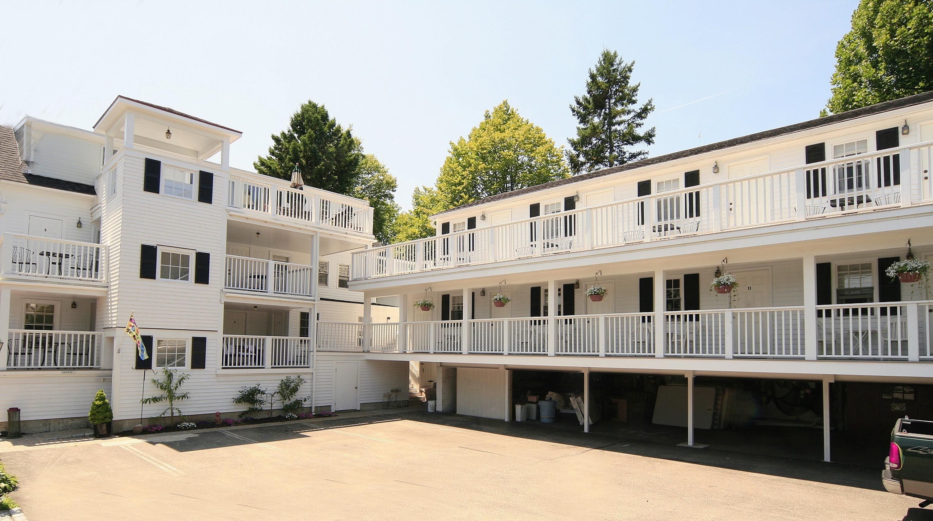 A two-story building with balconies, a covered front porch, and a parking area.