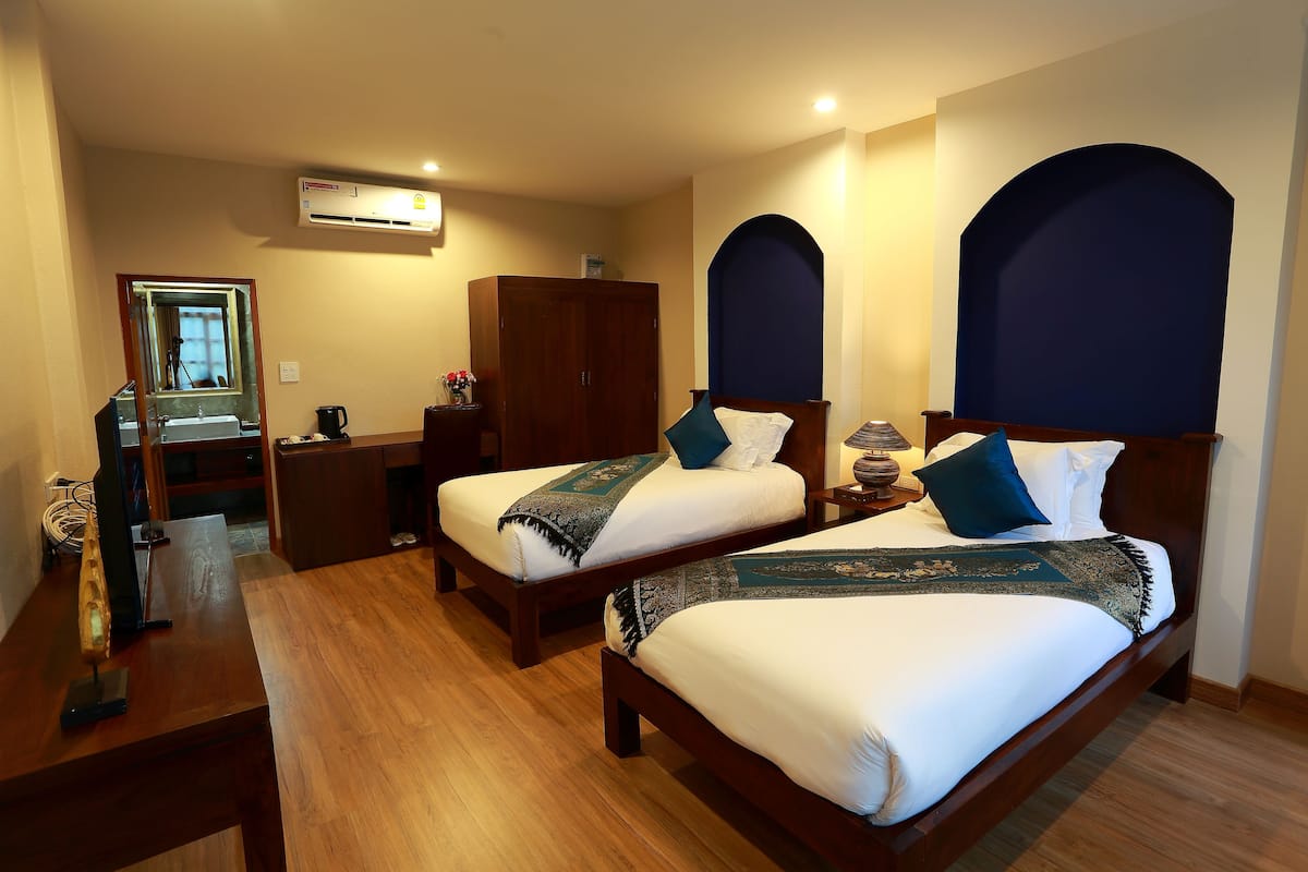 A hotel room with two beds, a desk, a wardrobe, and an air conditioning unit.