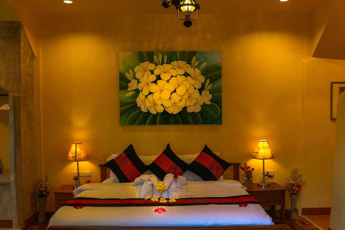 A hotel room with a large bed, two bedside lamps, a floral painting on the wall, and a wooden floor.