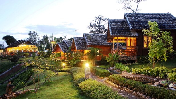 A row of traditional-style cottages with thatched roofs, surrounded by well-maintained gardens and a stone pathway. - E-outfitting Pai Resort (Pai)
