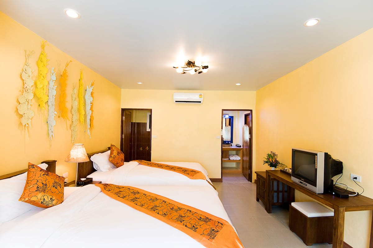 A hotel room with two beds, a TV, a desk, and a hallway leading to another room.