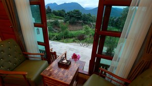 A room with a wooden table and chairs, a view of a mountainous landscape through large windows, and a small table with a vase of flowers. - E-outfitting Pai Resort (Pai)