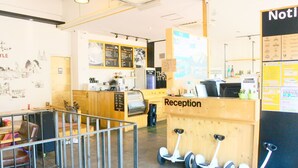A reception area with a wooden counter, a coffee machine, and a sign that reads "Reception." There are three segways parked in front of the counter. - The Style Capsule Guesthouse - Hostel (Daegu)