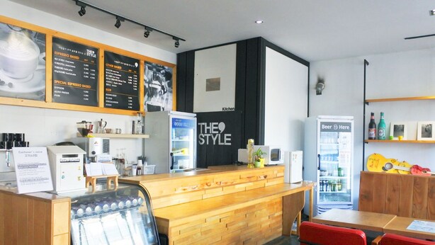 A coffee shop interior with a wooden counter, espresso machine, and menu boards. - The Style Capsule Guesthouse - Hostel (Daegu)