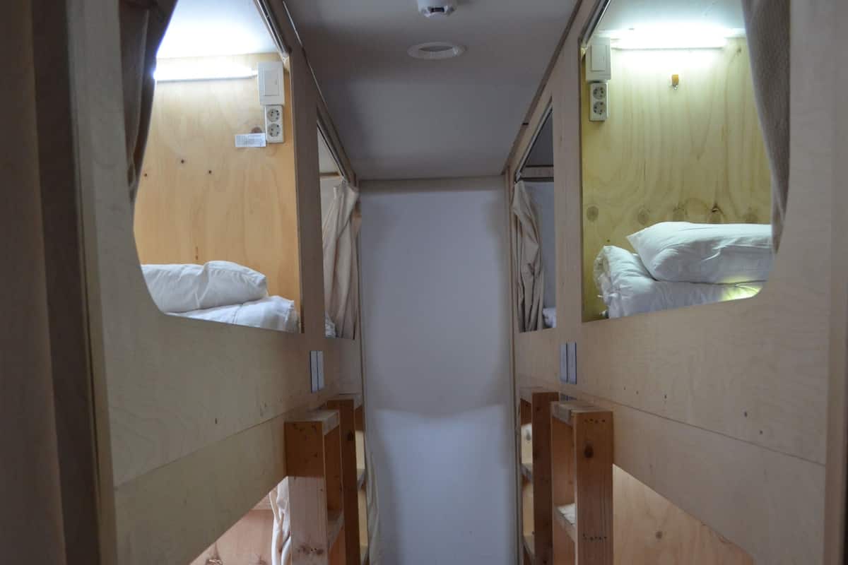 A narrow corridor with bunk beds on either side, wooden walls, and a red bed at the end.