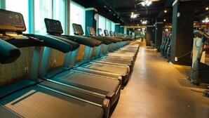 A row of treadmills in a gym with large windows and ceiling fans. - The Style Capsule Guesthouse - Hostel (Daegu)