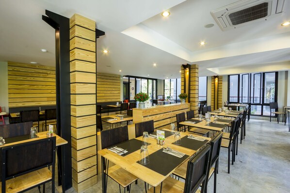 A modern dining area with wooden panel walls, black chairs, and tables set for service.
