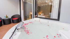 A modern bathroom with a large bathtub, a shower, and a glass-enclosed shower area. There are wicker chairs and a small table with a vase of flowers.