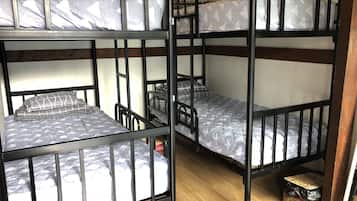 Une chambre avec un lit superposé à trois niveaux, un plancher en bois et un petit panier en osier placé sous le lit du bas.