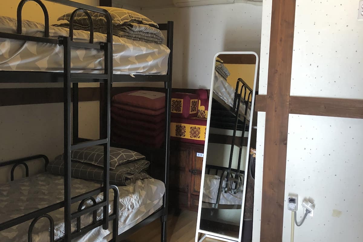 A bunk bed room with a wooden floor, a white wall with a small air conditioning unit, and a whiteboard.