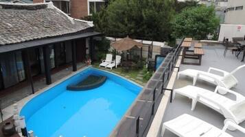 Une piscine sur le toit, avec une fontaine à eau d’un bleu cristallin, entourée de chaises longues blanches et d’un espace salon abrité.