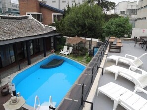 A rooftop swimming pool with a clear blue water feature, surrounded by white lounge chairs and a covered seating area.