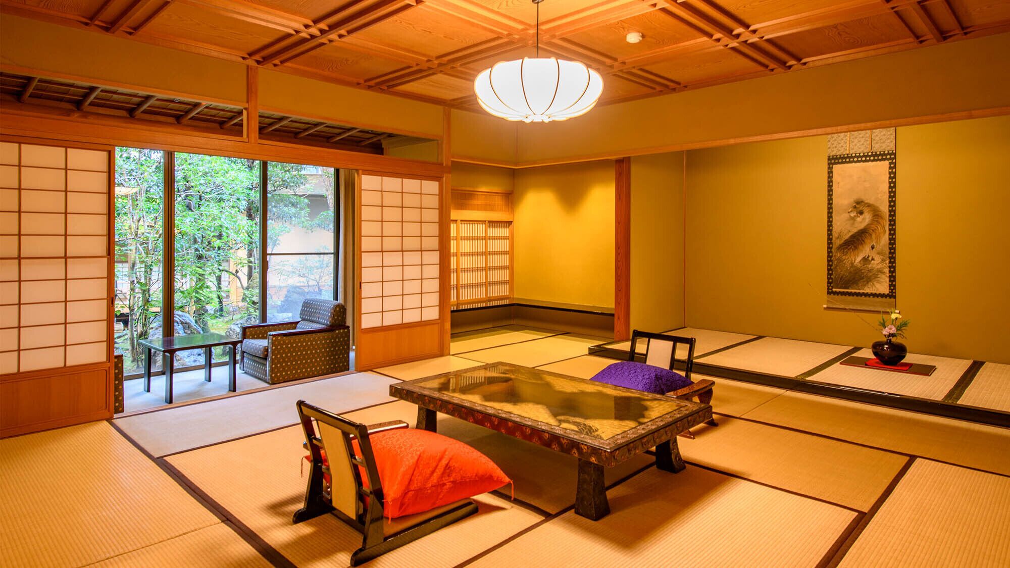 Una habitación japonesa tradicional con suelo de tatami, una mesa baja, una silla acolchada y puertas correderas que dan a un jardín.