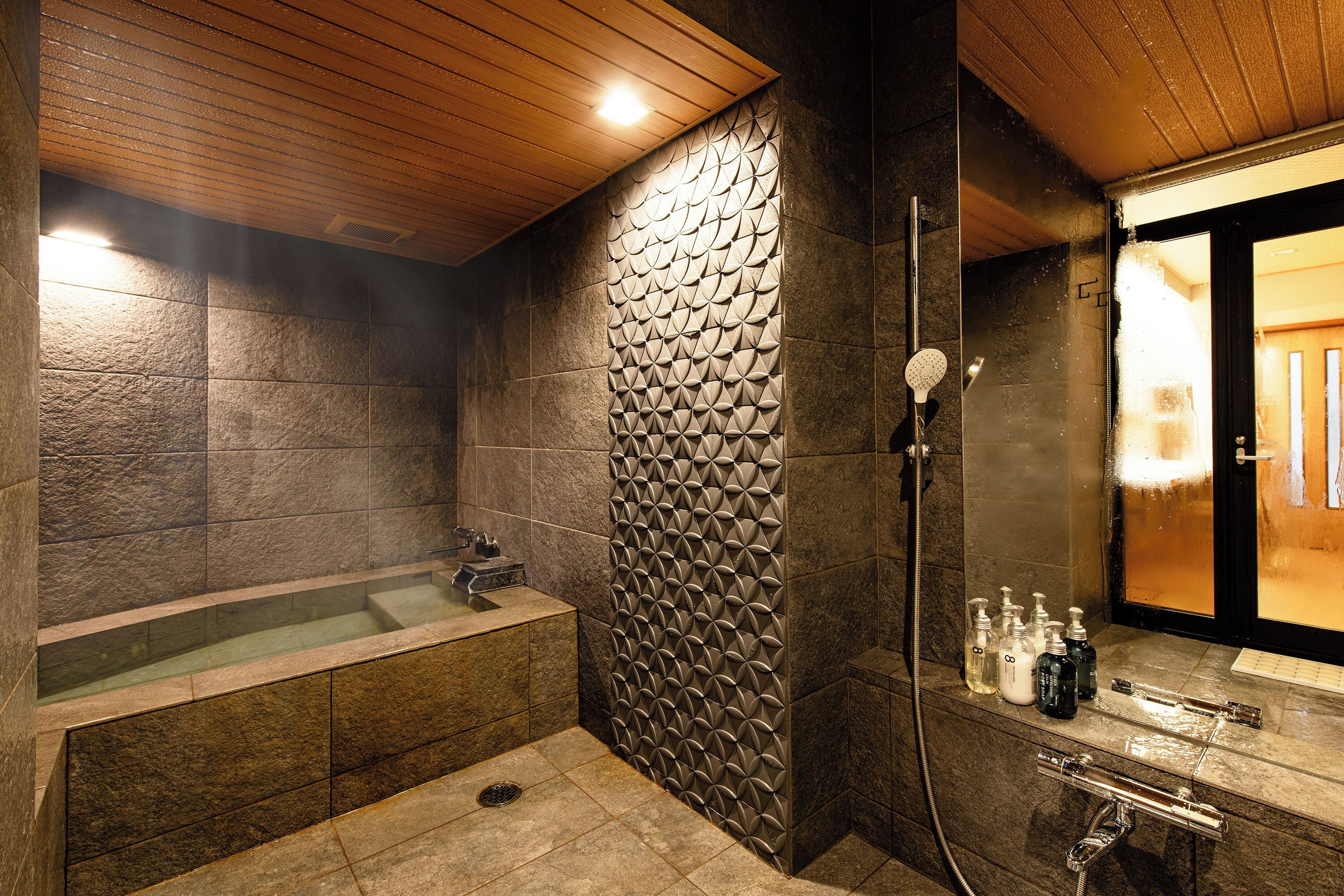 Une salle de bain moderne avec un mur en pierre, une baignoire et un espace douche.