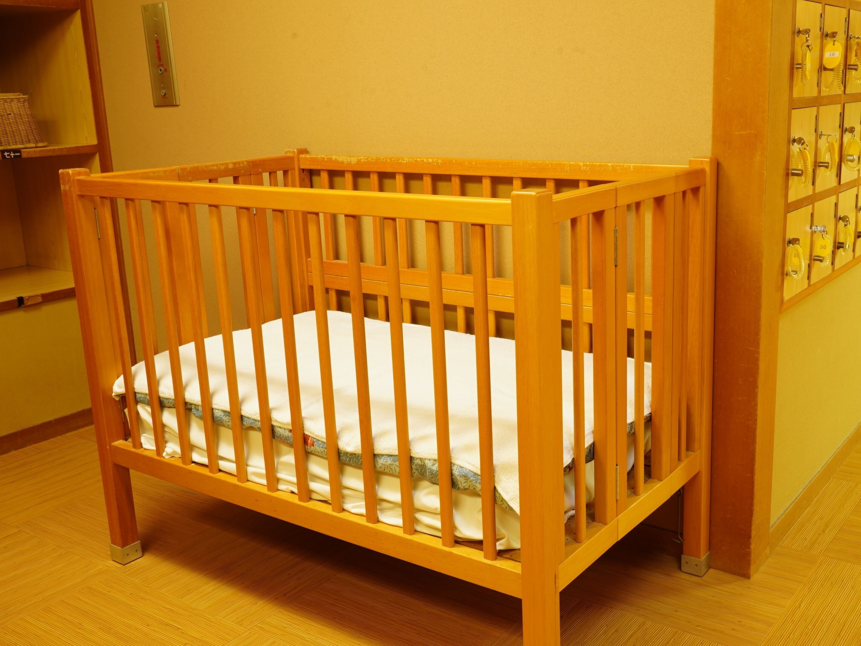 A wooden crib with a white mattress in a room with yellow walls and a wooden floor.