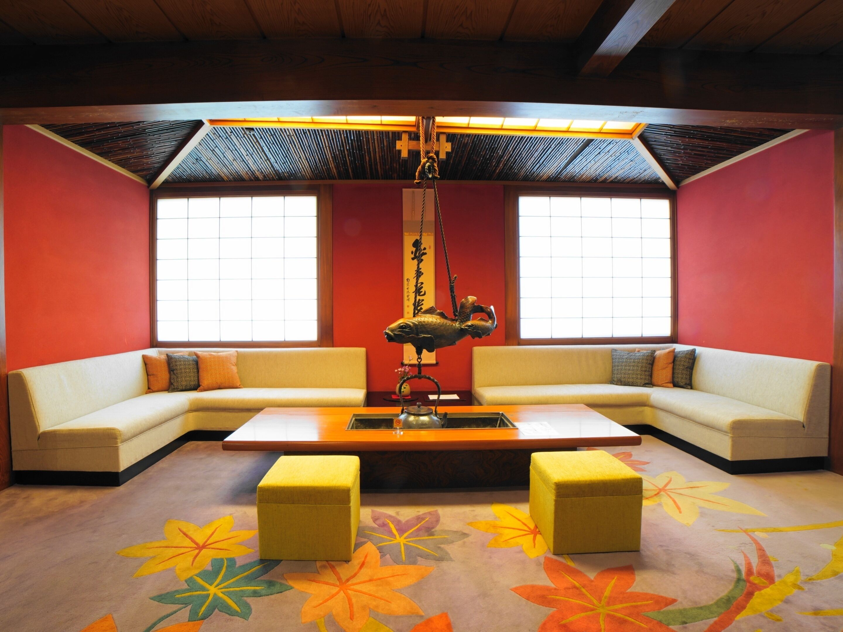 A room with a sofa, ottomans, a table, and a decorative hanging.