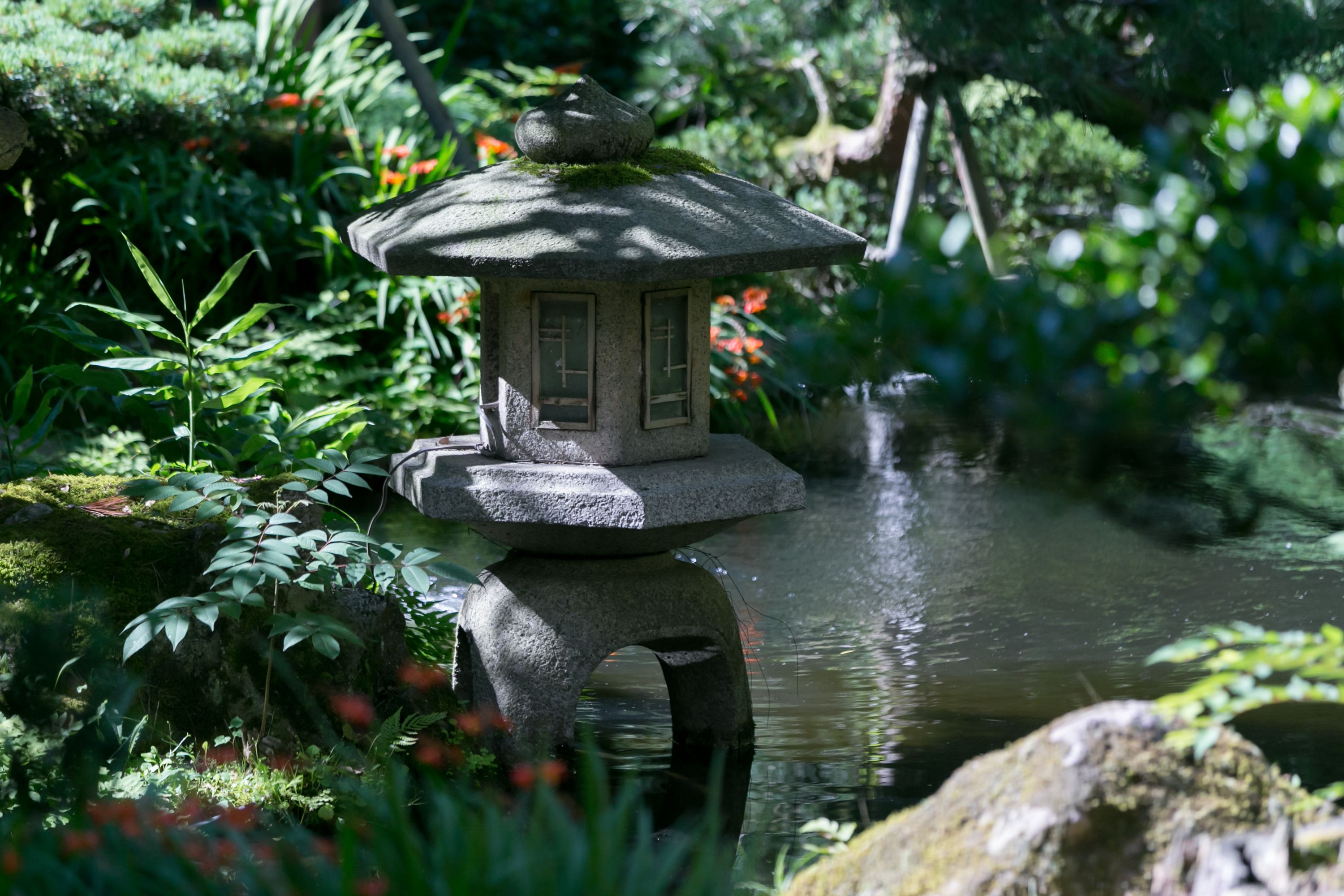 A stone lantern in a garden with a pond.