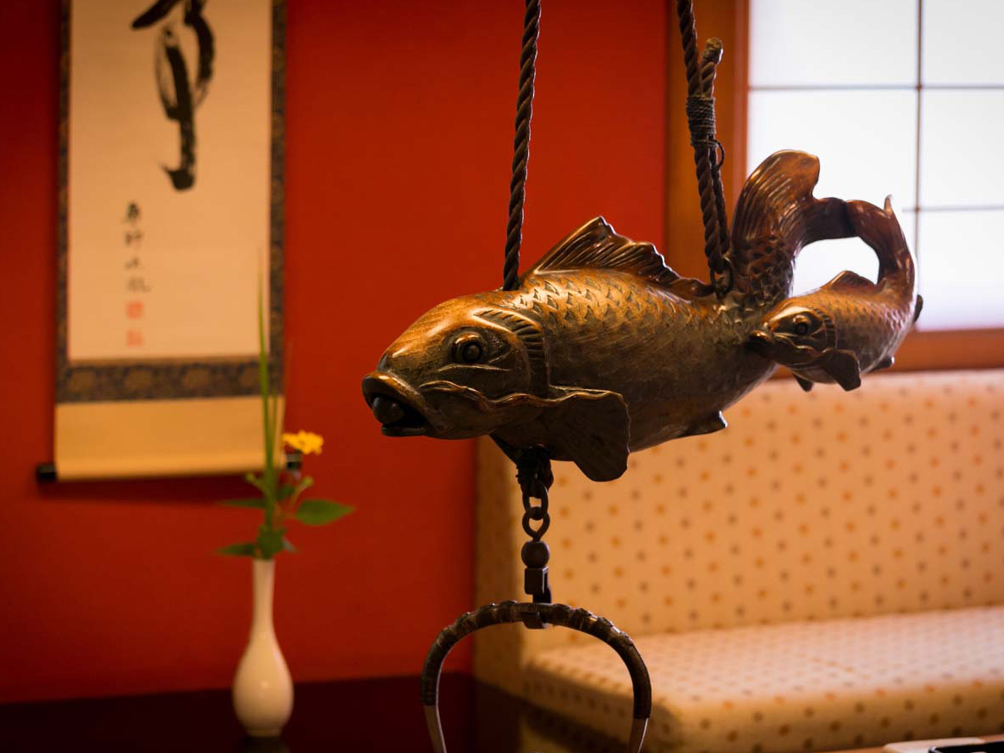 A fish-shaped hanging ornament in a room with a patterned sofa and a framed artwork on the wall.