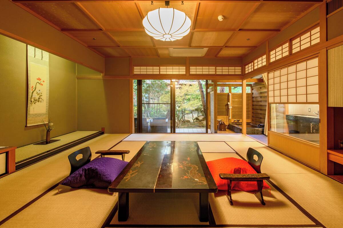 A traditional Japanese room with tatami flooring, a low table, and sliding doors leading to an outdoor area.