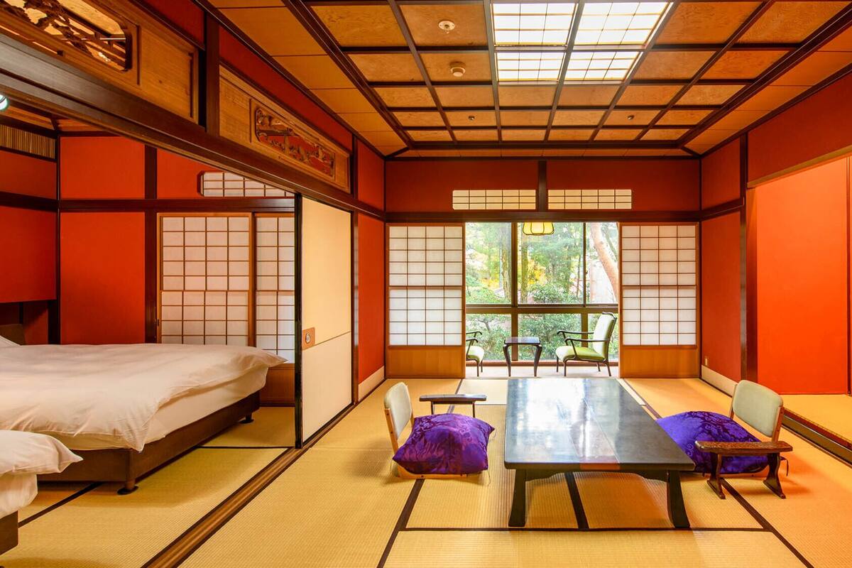 A traditional Japanese room with tatami flooring, a low table, chairs, and a bed.