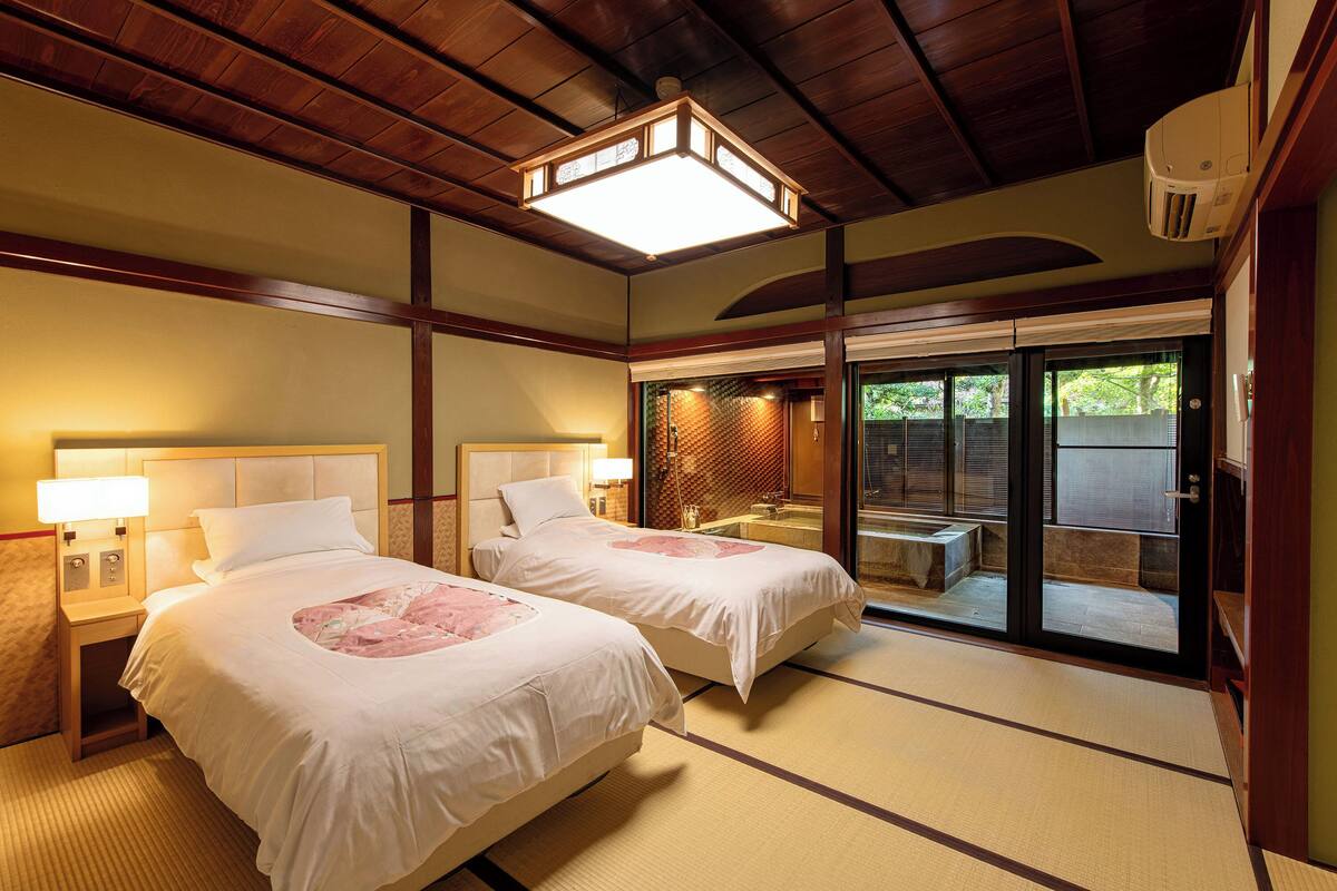 A hotel room with two beds, a large window, a ceiling fan, and a traditional Japanese tatami mat floor.