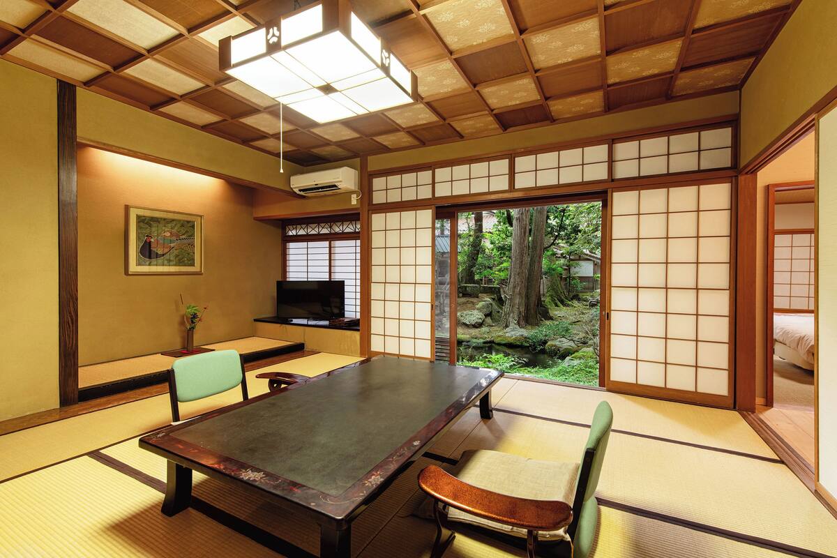 A traditional Japanese room with tatami flooring, a low table, and sliding doors leading to a garden.