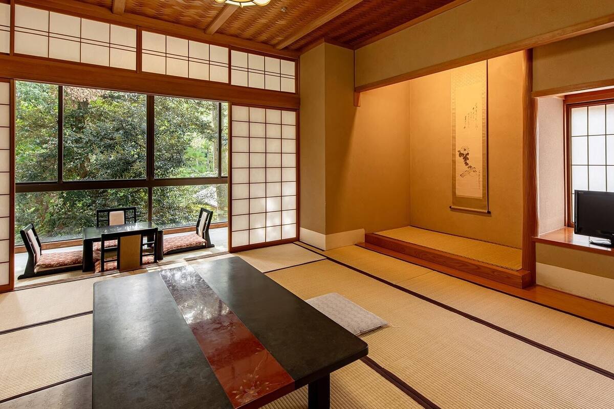 A traditional Japanese room with tatami flooring, a low table, a sofa, and a TV.